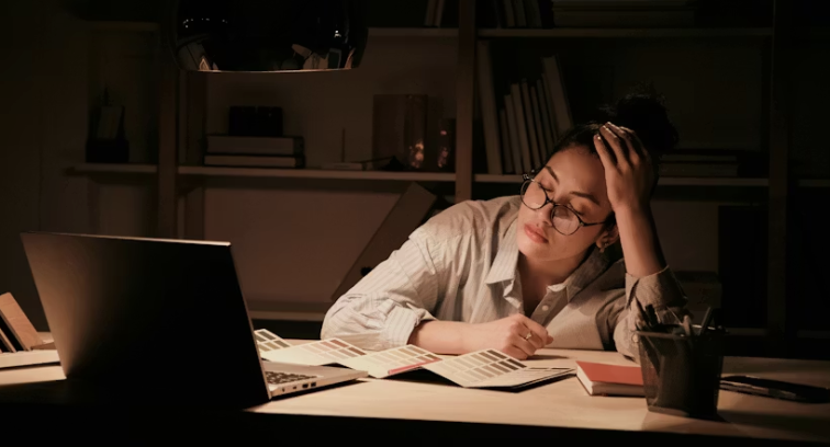 A woman working late at night under pressure, showing the emotional burden of gendered precarious work